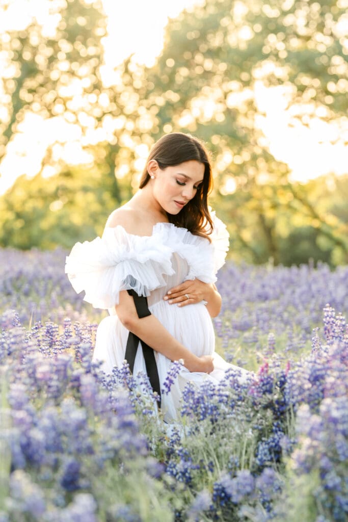 Pregnant mother in a white tulle gown walking through a lupine field during an El Dorado Hills maternity session