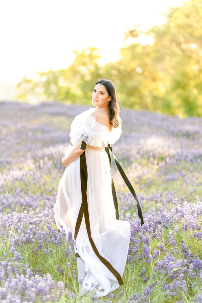 Expecting mother wearing a flowing white gown in a Northern California lupine wildflower field