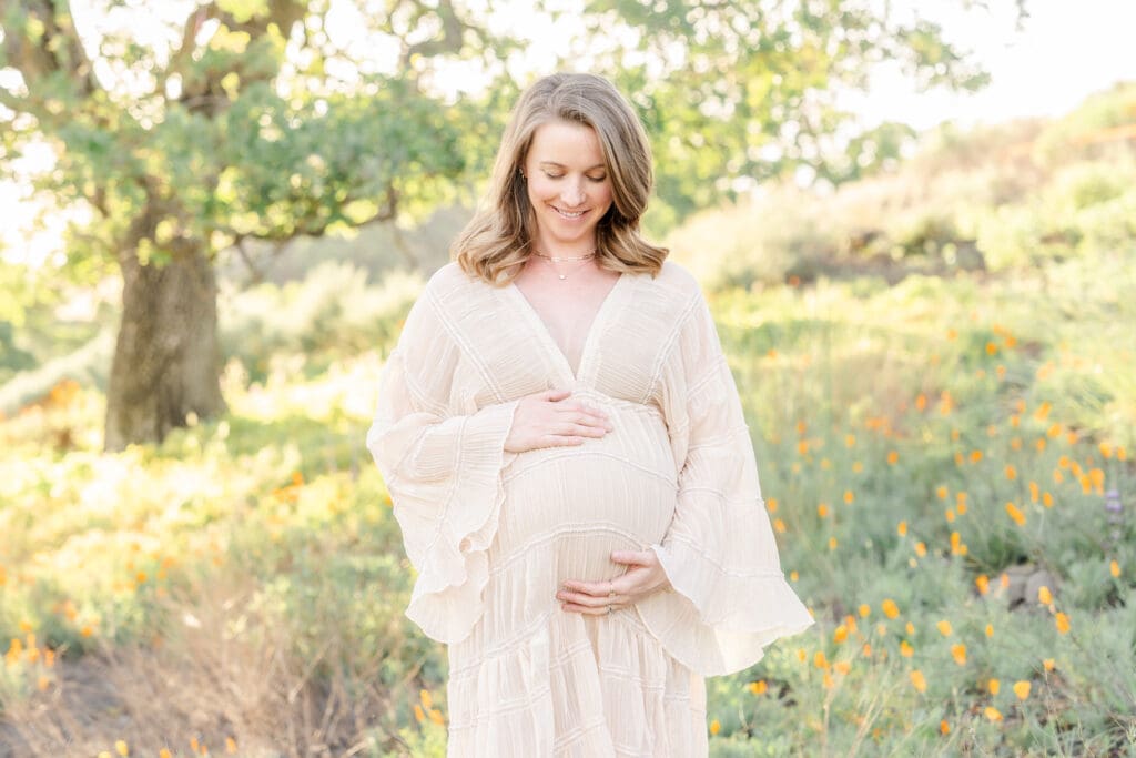 A expecting mom holding her belly in a Walnut Creek CA poppy field.