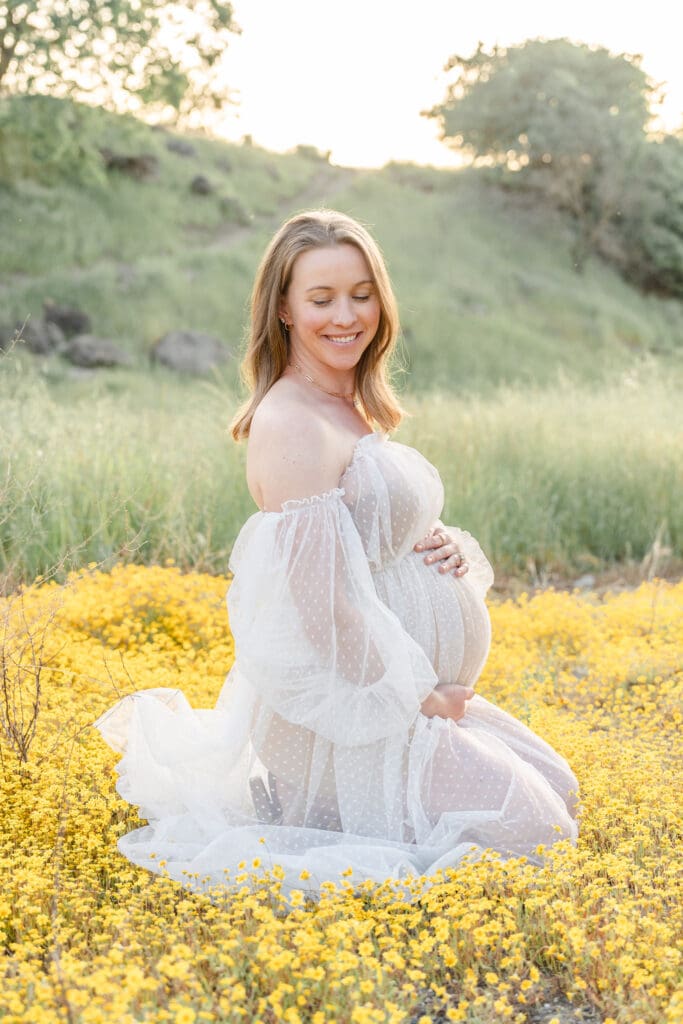 A mom in a white gown sitting on yellow flowers in Walnut Creek CA